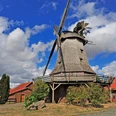 Meßlinger Mühle 2 Historische Windmühle mit grauen Schindeln, Holzgalerie und Flügeln vor blauem Himmel und Wolken.