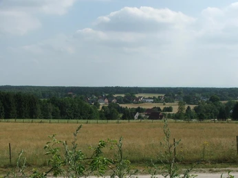 Blick in die Senne Landschaftsansicht mit Wiesen im Vordergrund, einem Dorf mittig und bewaldeten Hügeln im Hintergrund.