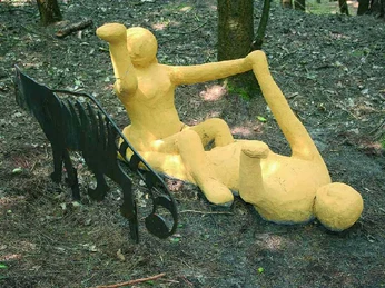 Freiraum Zwei gelbe Skulpturenfiguren liegen spielerisch im Wald neben einer abstrakten Metallform.