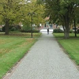 Sedanplatz Ein gepflasterter Weg führt durch einen grünen Park mit Bäumen, im Hintergrund ein Gebäude.