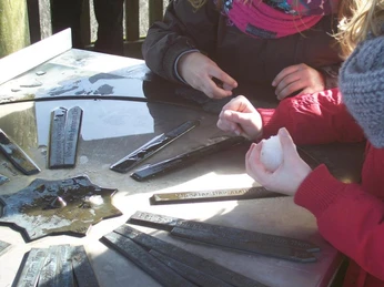 Kinder spielen mit Schnee und einer Sonnenuhr, umgeben von Metallstäben auf einer glatten Fläche.