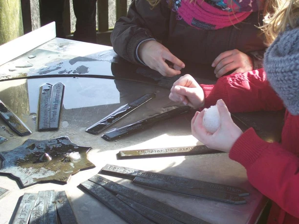 Kinder am Richtungsweiser, Luisenturm Borgholzhausen Kinder spielen mit Schnee und einer Sonnenuhr, umgeben von Metallstäben auf einer glatten Fläche.