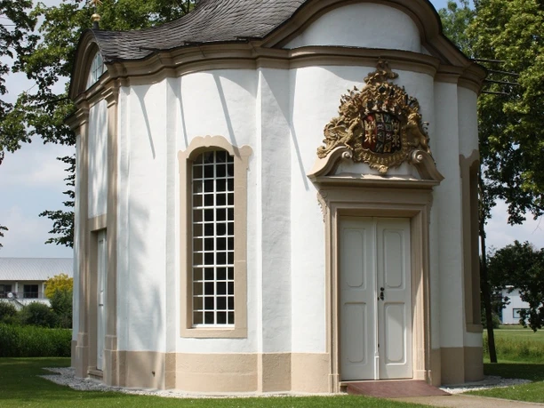 Johanneskapelle Kleine, barocke Kapelle mit weißer Fassade, geschwungenem Dach und barockem Wappen über der Tür.