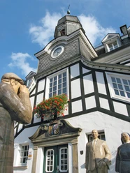 Historisches Fachwerkgebäude mit Turm und drei Statuen im Vordergrund unter klarem Himmel.
