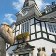 Historisches Fachwerkgebäude mit Turm und drei Statuen im Vordergrund unter klarem Himmel.