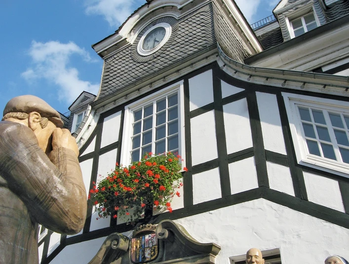 Historisches Fachwerkgebäude mit Turm und drei Statuen im Vordergrund unter klarem Himmel.