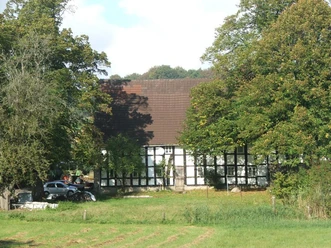 Hof Geers Fachwerkhaus umgeben von Bäumen und Wiesen, mit einem geparkten Auto auf der linken Seite.