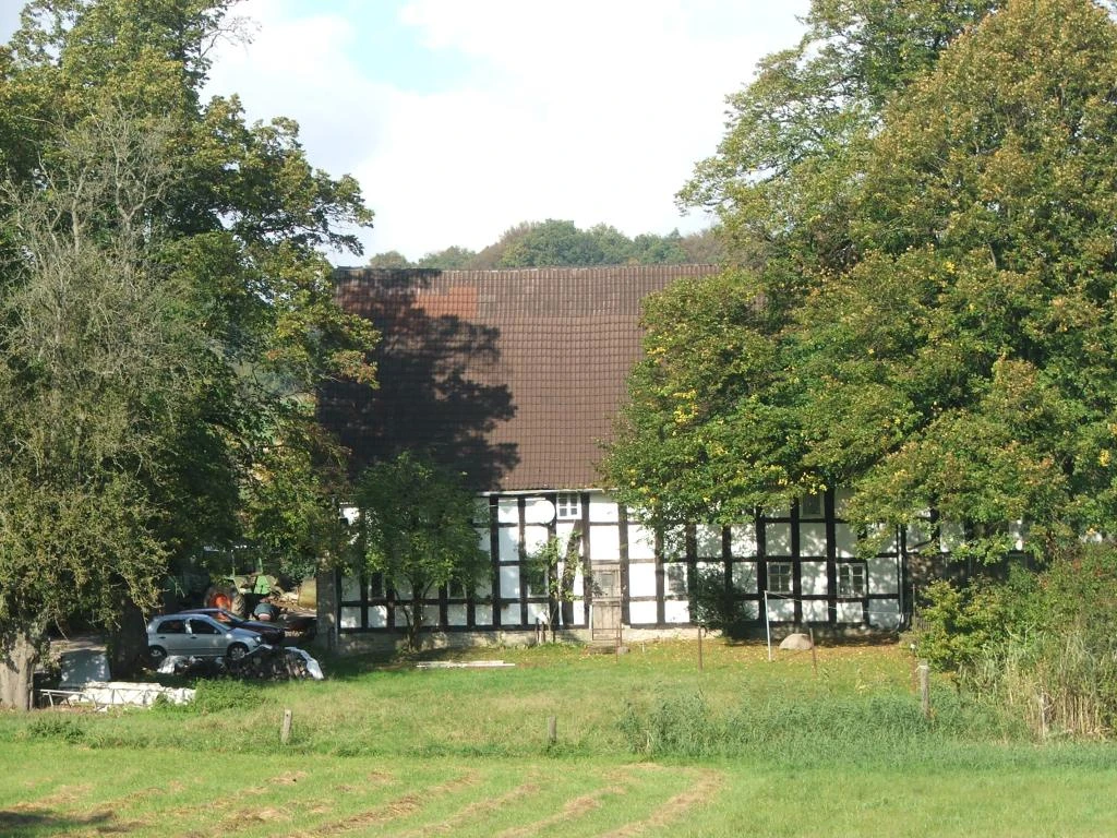 Hof Geers Fachwerkhaus umgeben von Bäumen und Wiesen, mit einem geparkten Auto auf der linken Seite.