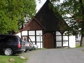 Fachwerkhaus Weberhof Fachwerkhaus mit weiß verputzten Wänden und dunklem Fachwerk, umgeben von Bäumen und Autos.