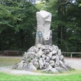 Steinerne Gedenksäule im Wald zu Ehren von Otto von Bismarck, umgeben von Bäumen und Kiesweg.