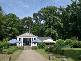 Parkvilla im Stadtpark Ein charmantes Café mit klassischem Säuleneingang, umgeben von üppigem Grün und mehreren Sonnenschirmen.