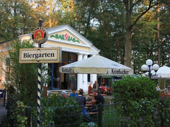 Parkvilla im Stadtpark Ein Biergarten im Grünen mit weißen Sonnenschirmen und einem Gebäude im Hintergrund bei Tageslicht.
