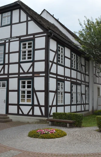 Fachwerkhaus mit weißen Wänden und dunklen Holzbalken, umgeben von gepflegten Grünanlagen.