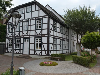 Haus des Gastes Fachwerkhaus mit weißen Wänden und dunklen Holzbalken, umgeben von gepflegten Grünanlagen.