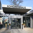 Kongresshaus Außenansicht Modernes Kongresshaus mit Glasfassade und automatischen Türen, umgeben von urbaner Umgebung.