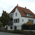 Haus Grotebrune Das weiße Haus Grotebrune mit rotem Ziegeldach steht an einer Straßenecke, flankiert von Bäumen.