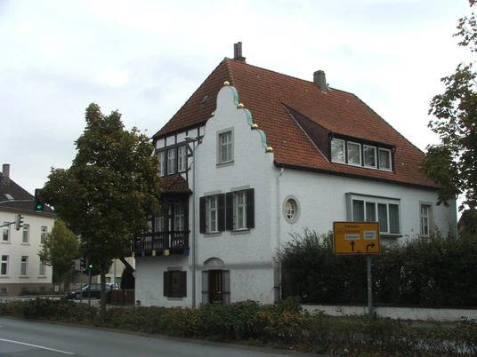 Haus Grotebrune Das weiße Haus Grotebrune mit rotem Ziegeldach steht an einer Straßenecke, flankiert von Bäumen.
