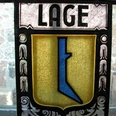 Wappen im Haus Grotebrune Buntes Bleiglasfenster mit einem Wappen, das ein abstraktes, blaues Symbol auf goldenen Hintergrund zeigt.