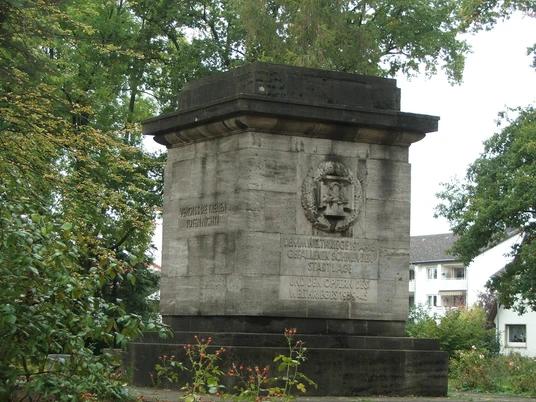 Gedenkstein aus Stein mit Inschrift, umgeben von Bäumen im Friedenspark, erinnert an historische Ereignisse.