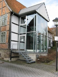 Stadtarchiv Modernes Glaseingangsportal mit Metalltreppe an einem historischen Fachwerkgebäude in städtischer Umgebung.