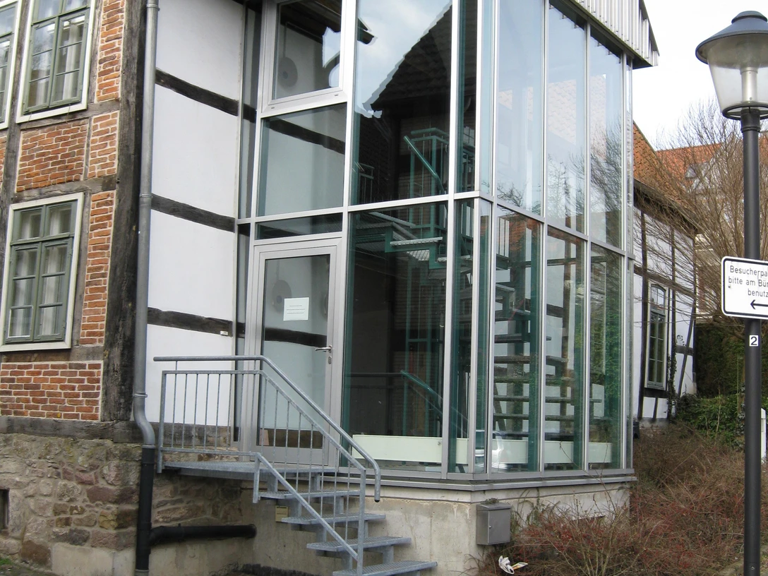 Stadtarchiv Modernes Glaseingangsportal mit Metalltreppe an einem historischen Fachwerkgebäude in städtischer Umgebung.