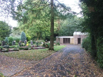Beschatteter Friedhofsweg mit Grabsteinen, leichter Laubbedeckung und angrenzender Kapelle.