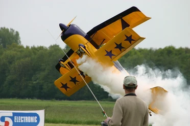 Flugmodelle: Spaß zum Bauen, Fliegen und Zuschauen Ein gelbes Kunstflugzeug im Steigflug mit weißem Rauch, beobachtet von einer Person im Vordergrund.