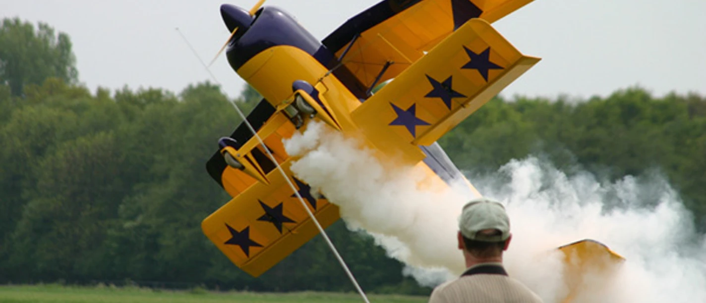 Flugmodelle: Spaß zum Bauen, Fliegen und Zuschauen Ein gelbes Kunstflugzeug im Steigflug mit weißem Rauch, beobachtet von einer Person im Vordergrund.