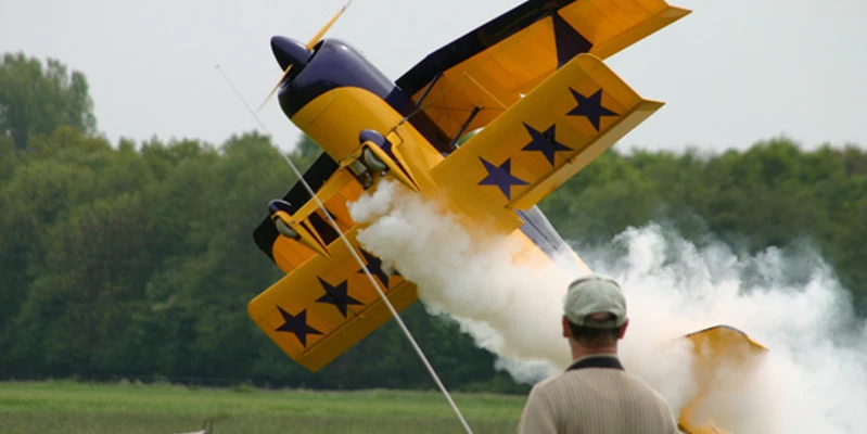 Flugmodelle: Spaß zum Bauen, Fliegen und Zuschauen Ein gelbes Kunstflugzeug im Steigflug mit weißem Rauch, beobachtet von einer Person im Vordergrund.