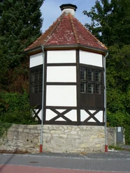 Luise-Hensel-Gartenhaus Fachwerkhaus mit achteckigem Grundriss und ziegelbedecktem Dach, umgeben von Bäumen und Sträuchern.