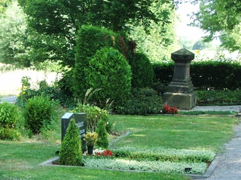 Friedhof Heiden Grüner Friedhof mit gepflegten Gräbern, Steinplatten und einem steinernen Denkmal im Sommerlicht.