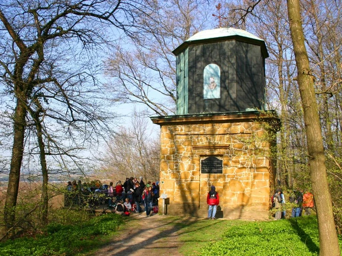 Eine Gruppe von Menschen steht vor einem steinernen Aussichtsturm im sonnigen Wald.