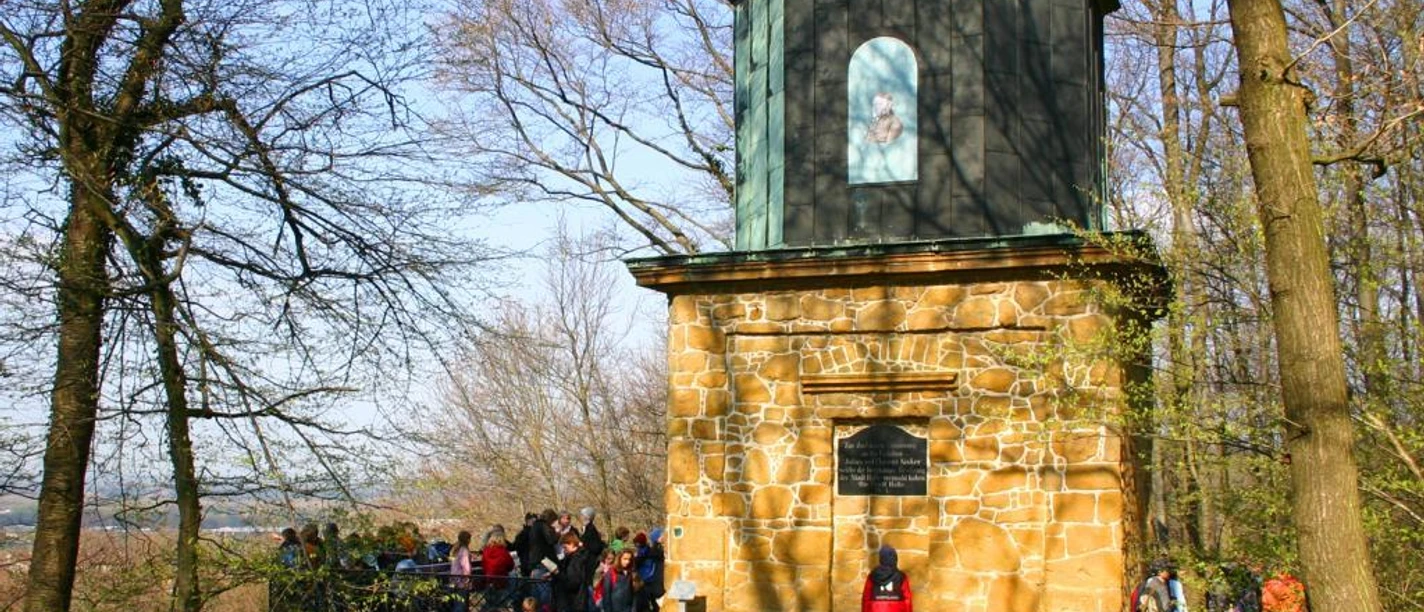 Kaffeemühle in Halle Westfalen am Hermannsweg Eine Gruppe von Menschen steht vor einem steinernen Aussichtsturm im sonnigen Wald.