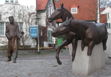 Halle Westfalen, Denkmal "Haller Willem" Zwei bronzene Pferdeskulpturen springen über Steinmauern, während ein Mann in Mantel sie beobachtet.