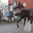 Halle Westfalen, Denkmal "Haller Willem" Zwei bronzene Pferdeskulpturen springen über Steinmauern, während ein Mann in Mantel sie beobachtet.