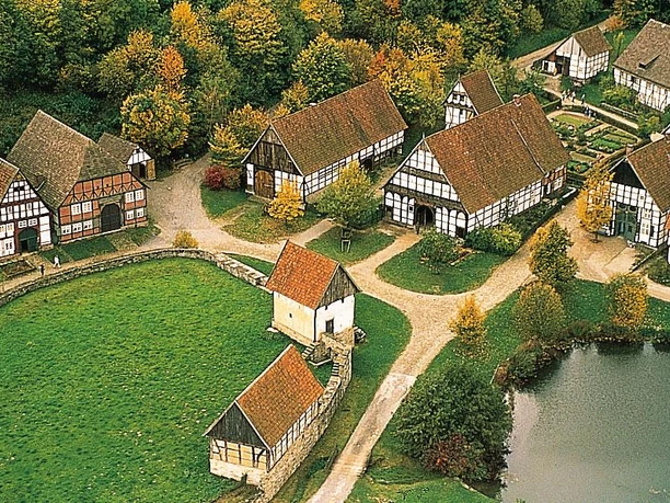 Luftansicht Luftaufnahme eines historischen Dorfes mit traditionellen Fachwerkhäusern, umgeben von Grünflächen.