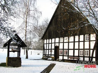 Heimathof im Winter Fachwerkhof im verschneiten Winterkleid, mit Brunnen im Vordergrund und schneebedeckten Bäumen.