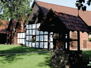 Heimathof Backhaus Traditionelles Fachwerkgebäude mit Backhaus und Ziehbrunnen, umgeben von grüner Rasenfläche.