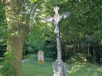 Hindahls Kreuz Lippspringer Wald Kruzifix im Lippspringer Wald, umgeben von dichten Bäumen, mit einem Grabstein im Hintergrund.