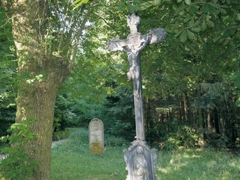 Hindahls Kreuz Lippspringer Wald Kruzifix im Lippspringer Wald, umgeben von dichten Bäumen, mit einem Grabstein im Hintergrund.
