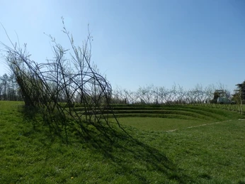 Skulpturenpark Lengerich Ein gewundener Weidenzaun umrahmt eine kreisförmige Rasenfläche mit terrassenartigen Stufen.