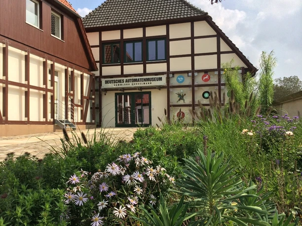 Deutsches Automatenmuseum Espelkamp - Aussenansicht Fachwerkgebäude mit grüner Gartenanlage und auffälligen Schildern des Deutschen Automatenmuseums.