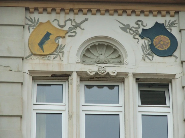 Fassade mit verzierter Wappendarstellung und geschnitzten Akzenten über zwei weißen Fenstern.