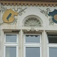 Rathaus II Fassade mit verzierter Wappendarstellung und geschnitzten Akzenten über zwei weißen Fenstern.