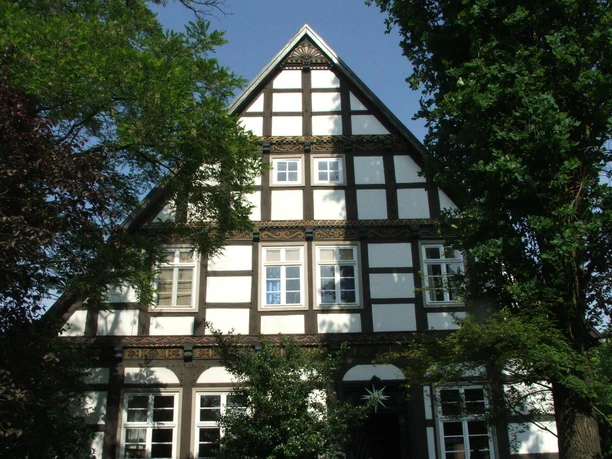 Fachwerkhaus Seppmann mit markantem Giebeldach, umgeben von üppig grünem Laubwerk bei Sonnenschein.