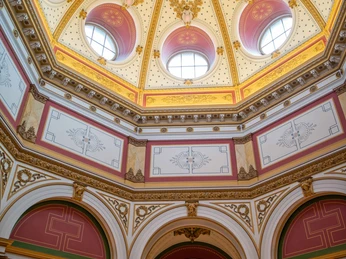 Das Bild zeigt eine kunstvolle Decke mit einem besonderen Muster in Beige-, Senfgelb- und Rottönen.