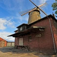 Historische Pottmühle aus rotem Backstein mit hölzernen Flügeln und angrenzendem Schuppen.