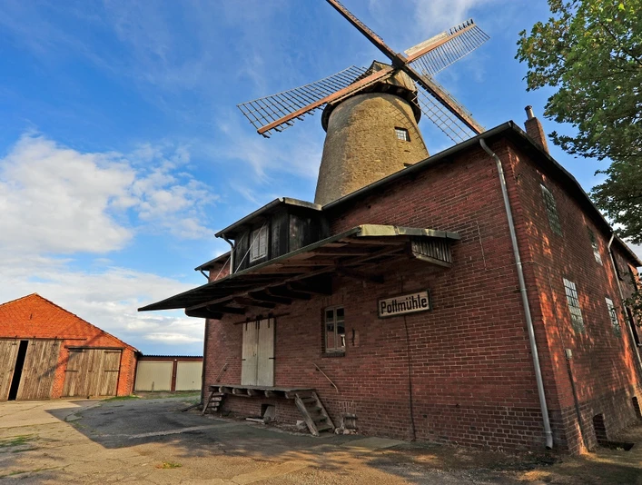 Historische Pottmühle aus rotem Backstein mit hölzernen Flügeln und angrenzendem Schuppen.
