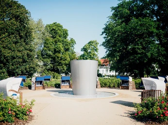Staatsbad Salzuflen - Strandkörbe am Solestrand Strandkörbe umringen einen modernen Springbrunnen, eingebettet in einen grünen Park voller Bäume.
