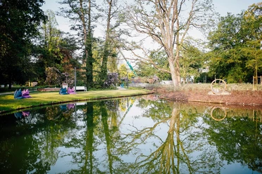 Staatsbad Salzuflen - Kurparksee Kurparksee in Bad Salzuflen mit klarer Wasseroberfläche, die üppige Bäume und Sitzgelegenheiten spiegelt.